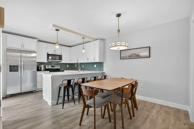 a kitchen with stainless steel appliances granite countertop a dining table chairs refrigerator and microwave