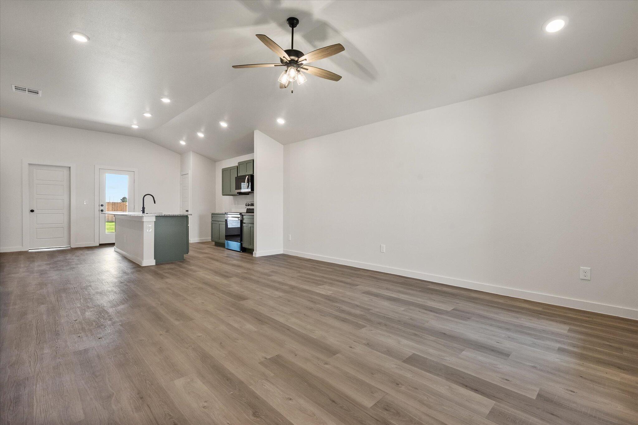 7215 8th Street Lubbock, TX 79416 - Photo 4 of 21 an empty room with wooden floor ceiling fan and kitchen view
