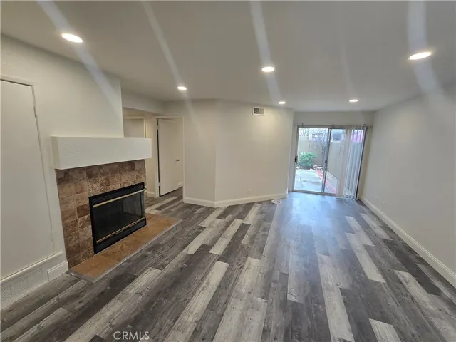 a view of an empty room with wooden floor fireplace and a window