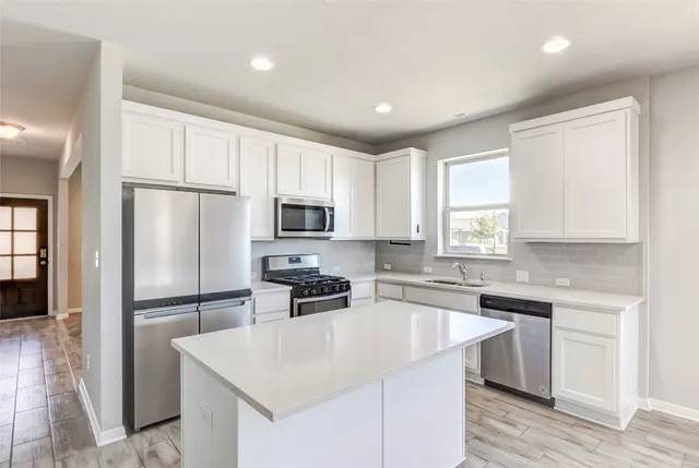 a kitchen with stainless steel appliances a stove top oven a sink a refrigerator white cabinets and wooden floor