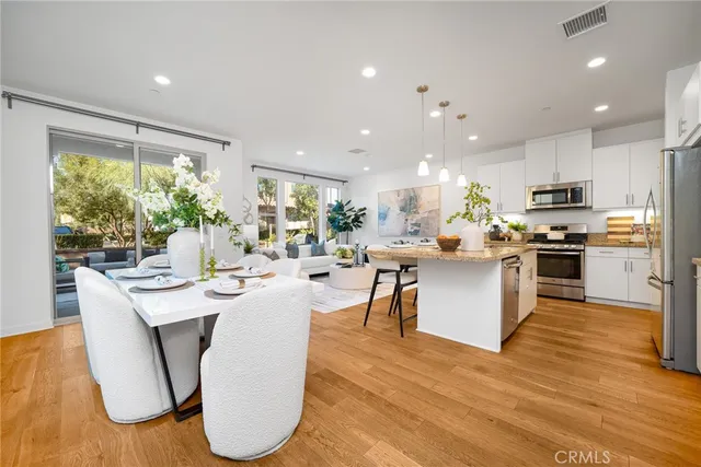 a living room with stainless steel appliances kitchen island granite countertop a table chairs and a wooden floor