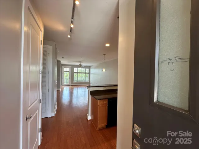 a view of a hallway to an empty room with wooden floor and a window