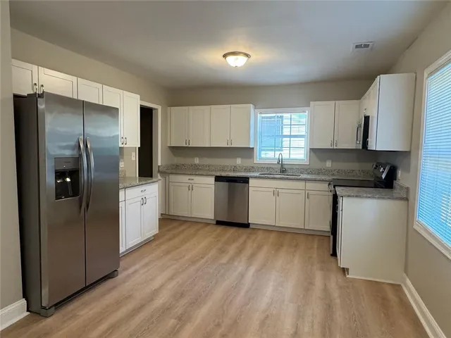 a kitchen with stainless steel appliances granite countertop a refrigerator a sink dishwasher a s stove top oven a large island with white cabinets and wooden floor