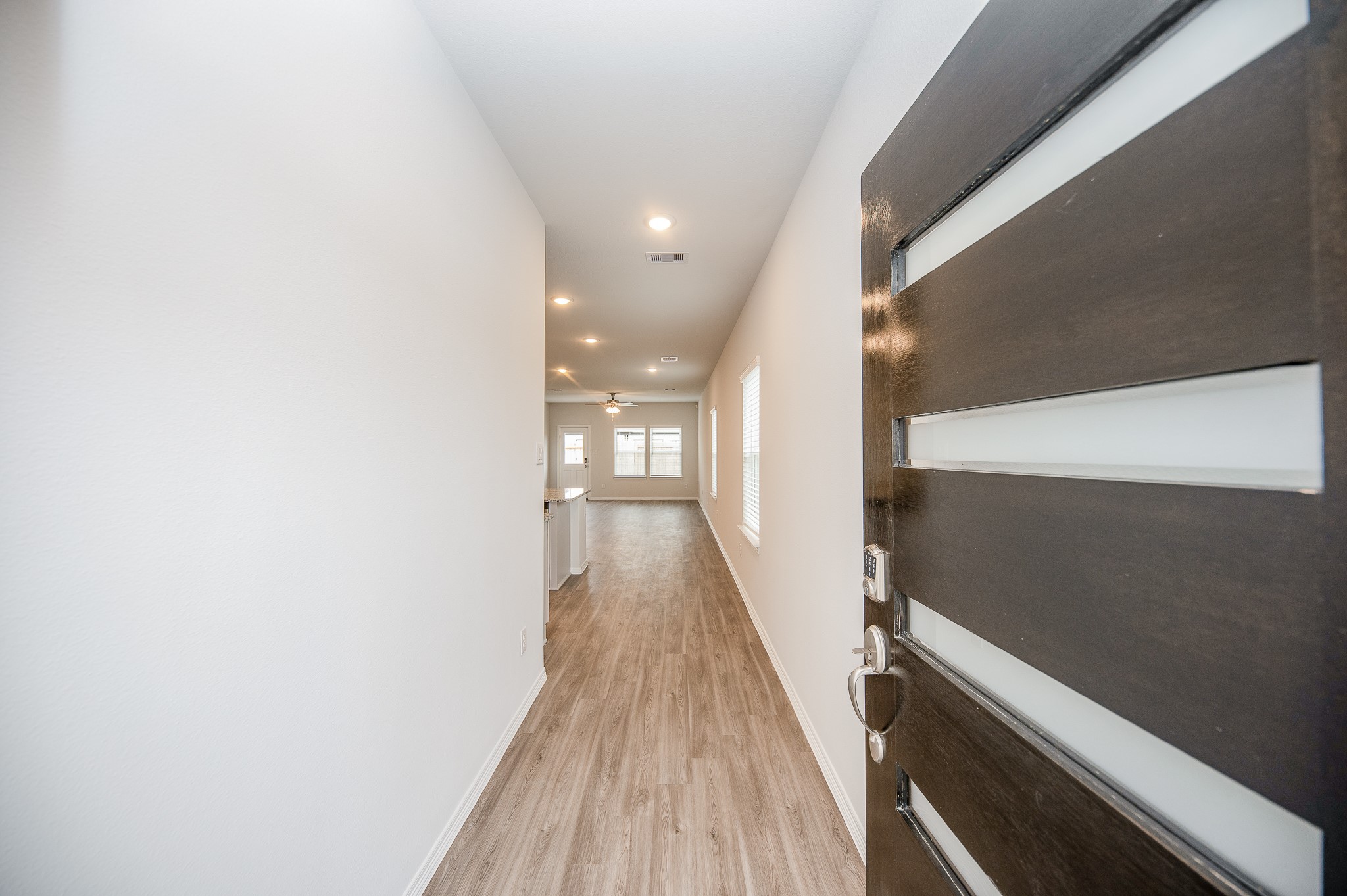 23302 Spring Genesis Lane Katy, TX 77493 - Photo 7 of 32 Modern entryway with a sleek, dark wooden door featuring horizontal glass panels. The hallway has light-colored walls and wood flooring, leading to a spacious, well-lit living area.