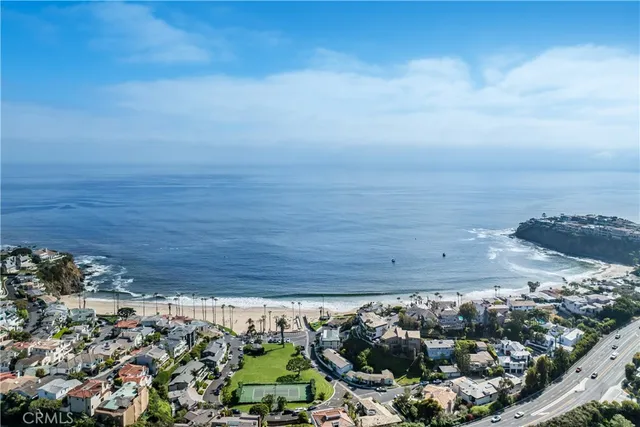 a white house with a small yard and large trees with potted plants