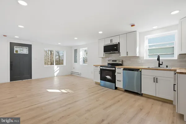 a kitchen with granite countertop a stove top oven a sink a refrigerator and white cabinets with wooden floor