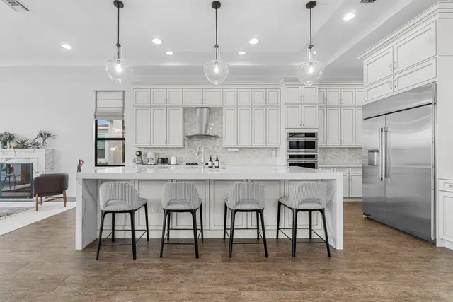 a kitchen with stainless steel appliances kitchen island granite countertop a stove a sink a microwave a refrigerator and white cabinets with wooden floor