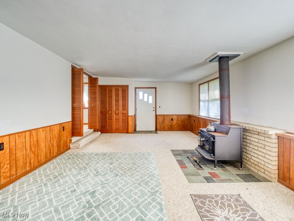 27133 Capel Road Columbia Station, OH 44028 - Photo 32 of 48 Unfurnished living room featuring carpet floors, a wood stove, a wainscoted wall, and wood walls