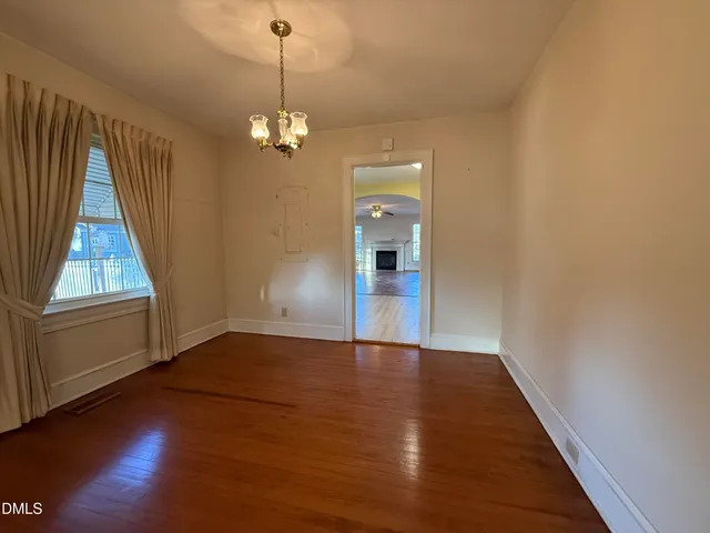 an empty room with wooden floor chandelier and windows