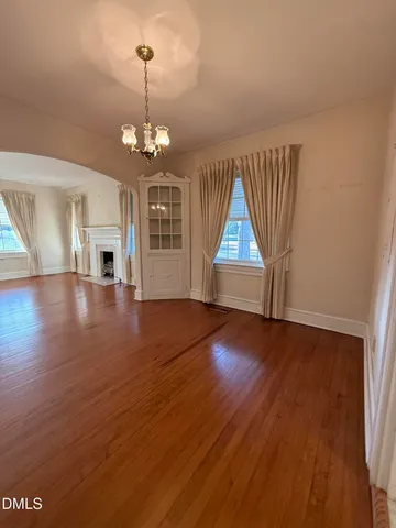 an empty room with wooden floor chandelier and windows