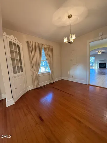 an empty room with wooden floor chandelier and windows