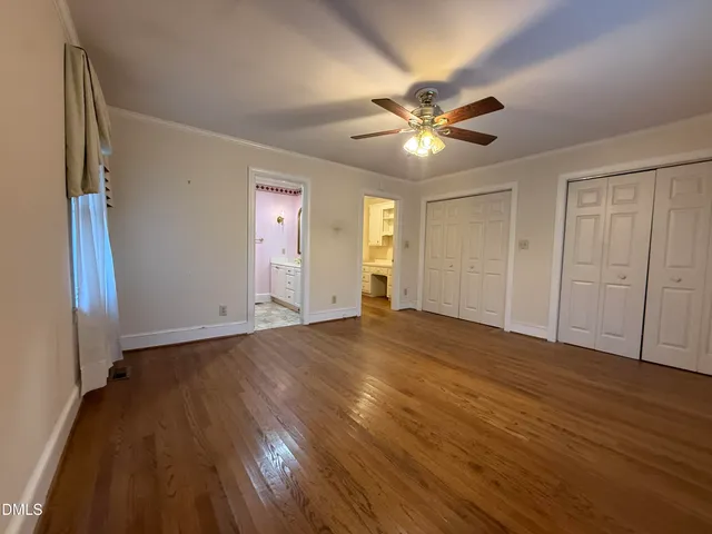 a view of an empty room with wooden floor and a ceiling fan