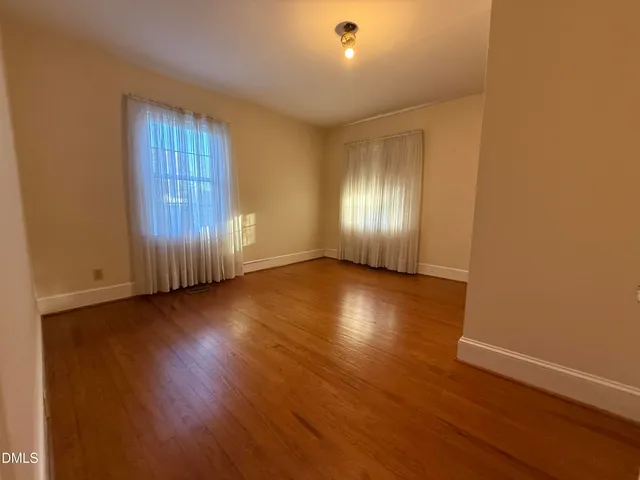 an empty room with wooden floor and windows with curtains