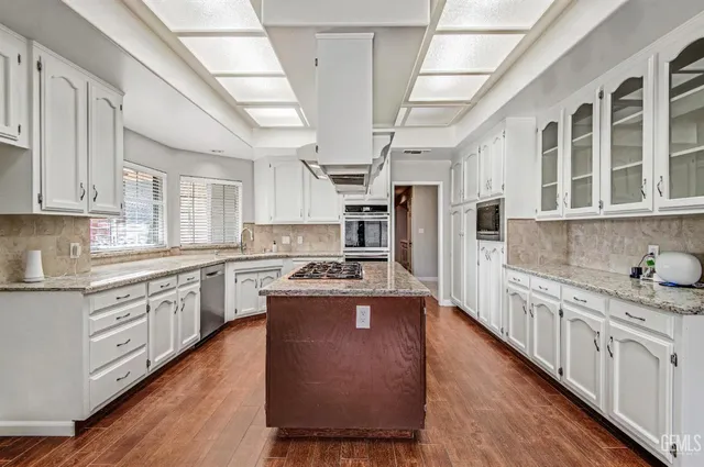 a kitchen with stainless steel appliances granite countertop a stove a sink dishwasher a refrigerator and white cabinets with wooden floor