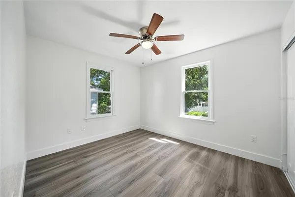an empty room with wooden floor windows and fan