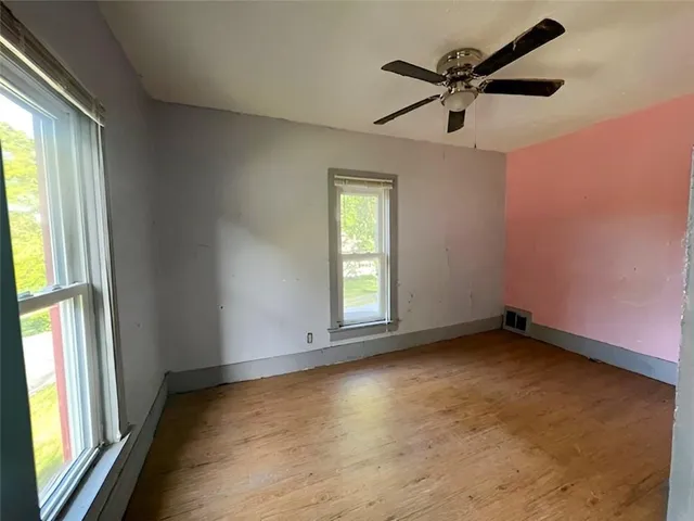 an empty room with wooden floor fan and windows