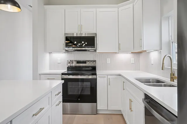 a kitchen with stainless steel appliances granite countertop white cabinets a stove and a sink