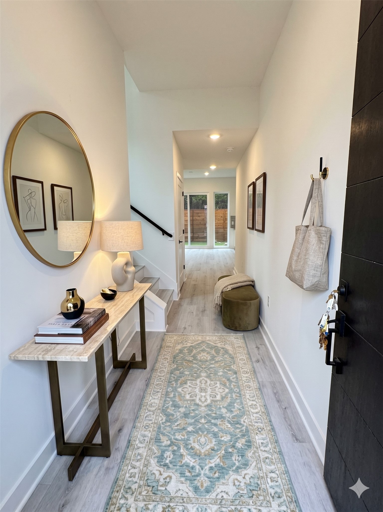 2000 Riverside Farms Road, Unit 19102 Austin, TX 78741 - Photo 3 of 13 This photo showcases a bright and inviting entryway with light wood flooring and a runner rug. There's a stylish console table with decor, a round mirror, and a lamp. The hallway leads to a glass door with backyard views, enhancing natural light.