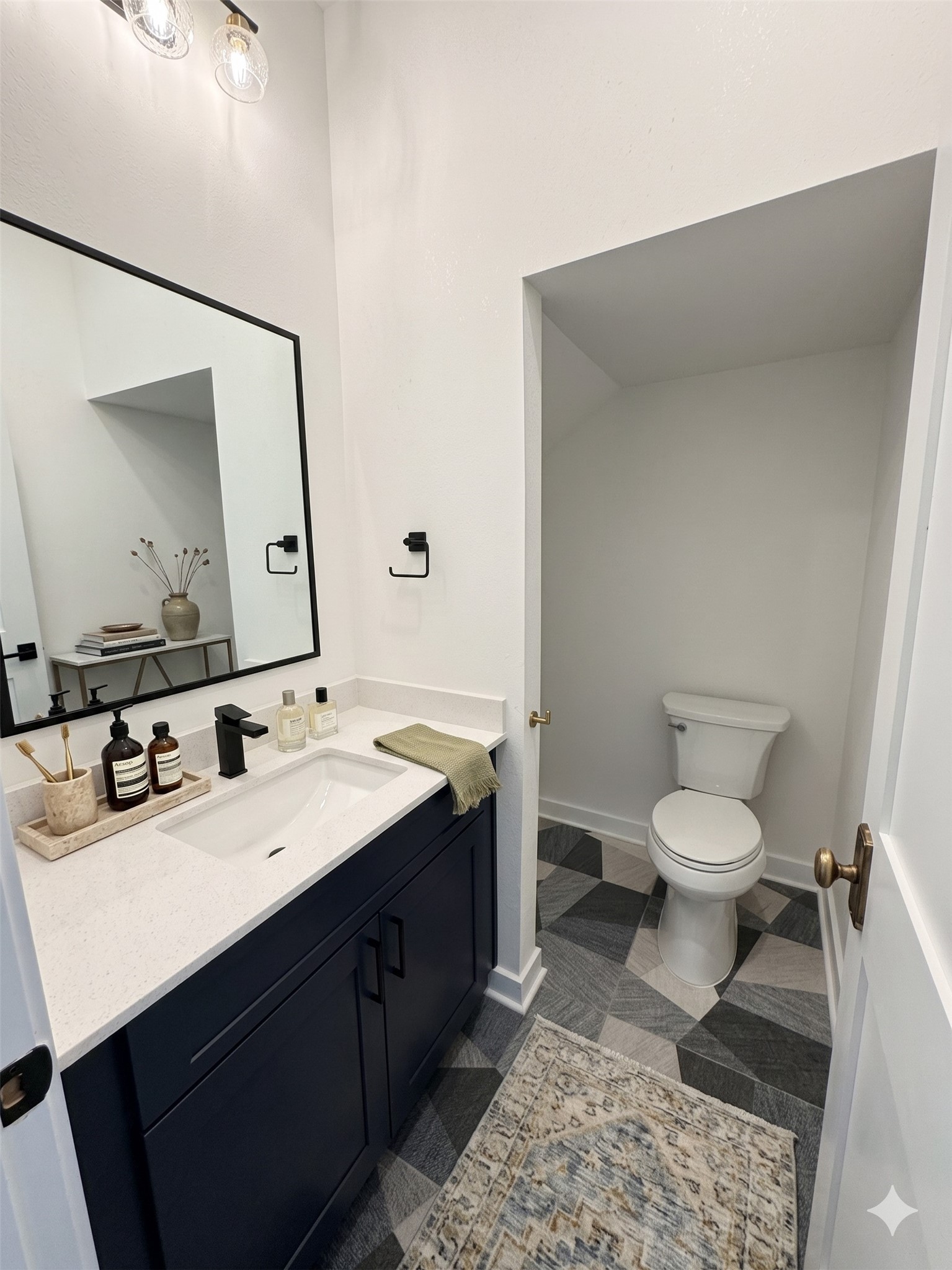 2000 Riverside Farms Road, Unit 19102 Austin, TX 78741 - Photo 10 of 13 This is a modern bathroom featuring a sleek dark vanity with a white countertop, a large mirror, and stylish geometric floor tiles. The space includes a separate area for the toilet, creating a clean and contemporary look.
