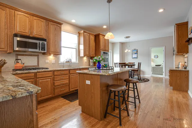 a kitchen with stainless steel appliances granite countertop a stove top oven a sink dishwasher a dining table and chairs with wooden floor