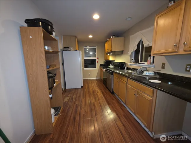 a kitchen with stainless steel appliances granite countertop a refrigerator a sink dishwasher a stove and white countertops with wooden floor