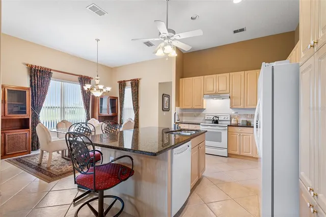 a kitchen with stainless steel appliances kitchen island granite countertop a refrigerator a sink dishwasher a dining table and chairs with wooden floor