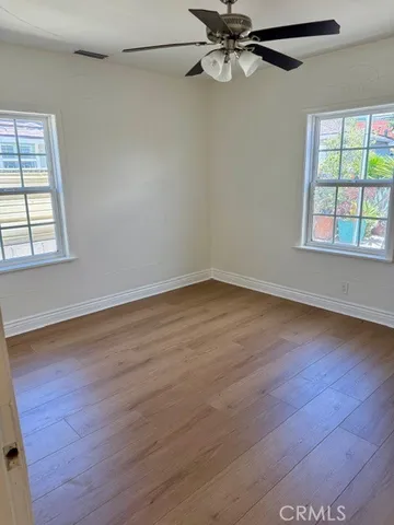 an empty room with wooden floor fan and windows