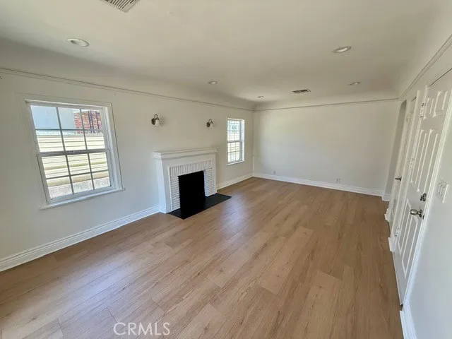 an empty room with wooden floor fireplace and windows