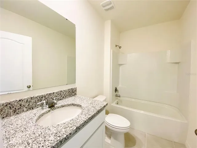 a bathroom with a granite countertop sink a toilet a mirror and bathtub