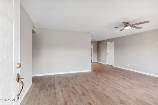 a view of an empty room with wooden floor and a ceiling fan