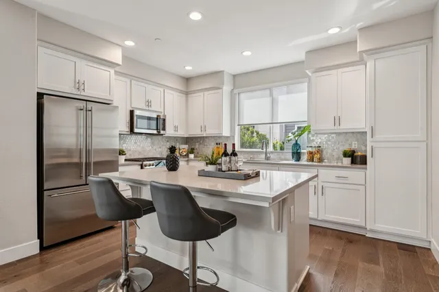 a kitchen with stainless steel appliances granite countertop a refrigerator a stove a sink and white cabinets with wooden floor