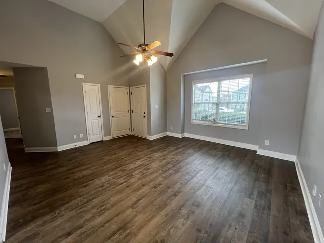 an empty room with wooden floor chandelier fan and windows