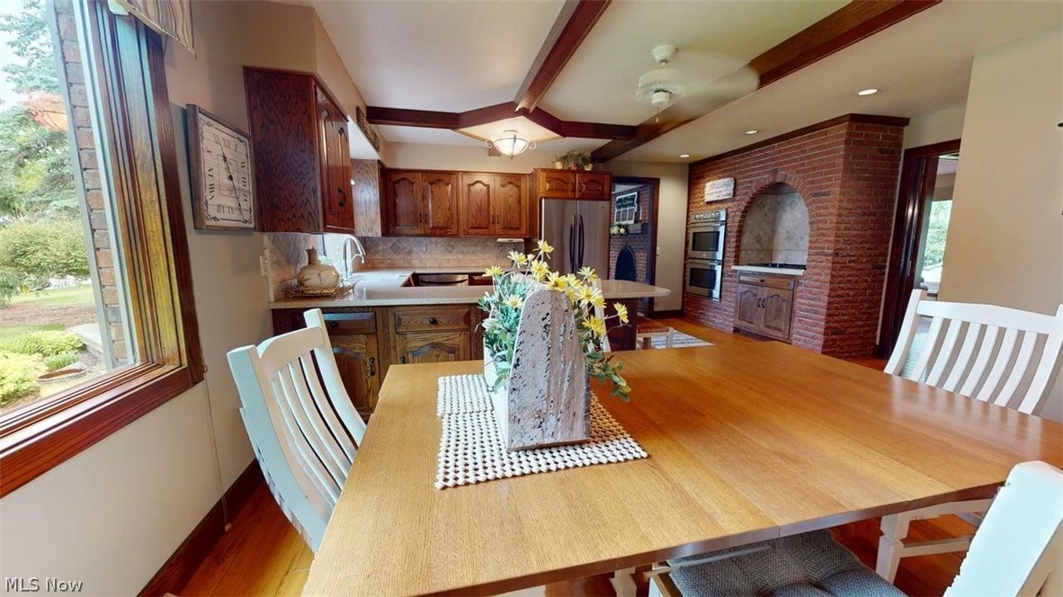 3985 Wiers Road Willard, OH 44890 - Photo 14 of 50 Kitchen area featuring wood-finish flooring, exposed ceiling beams, and a brick accent wall with a built-in oven and microwave