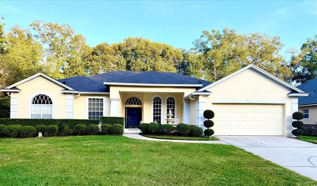 a view of a yard in front of a house with plants and large tree