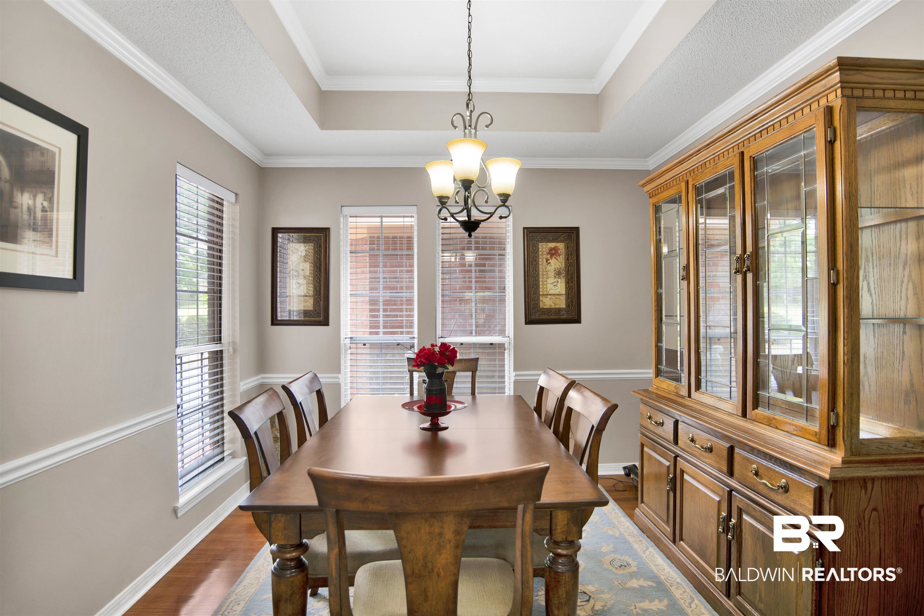 107 Virginia Circle Daphne, AL 36526 - Photo 7 of 47 Dining area featuring a tray ceiling with crown molding, a hanging chandelier, and two windows with blinds