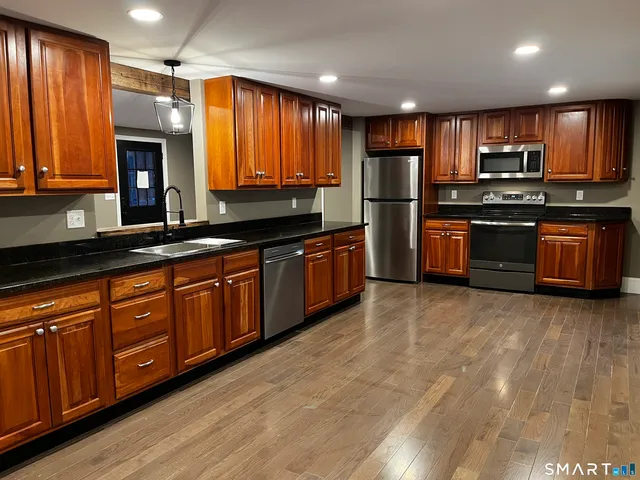 a kitchen with stainless steel appliances granite countertop wooden cabinets a refrigerator a stove a sink and dishwasher with wooden floor