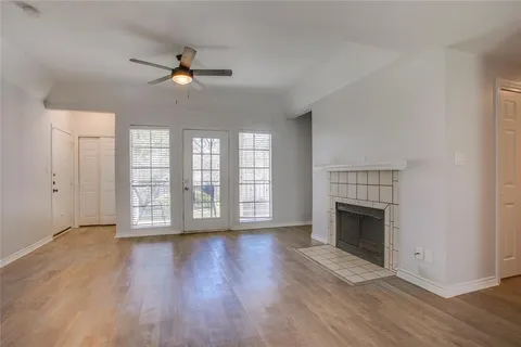 a view of an empty room with wooden floor fireplace and a window