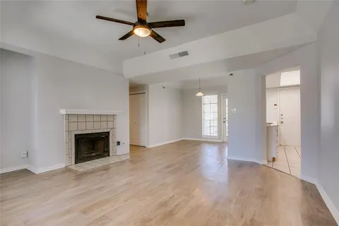 an empty room with wooden floor a ceiling fan a fireplace and windows