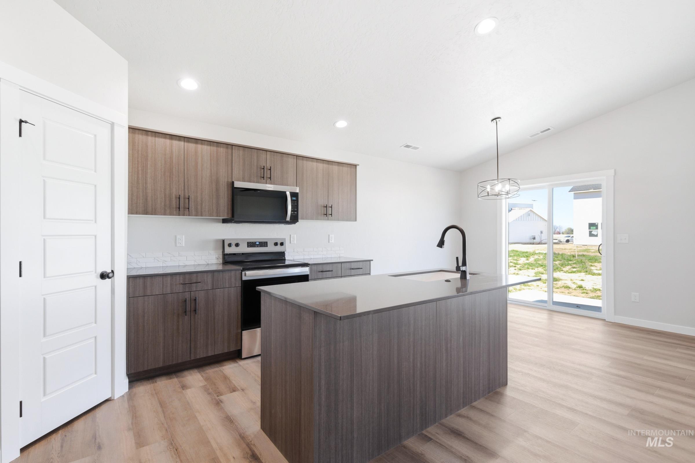 12805 Decatur Street Nampa, ID 83651 - Photo 4 of 20 Contemporary kitchen featuring wood-finish cabinetry, stainless steel appliances, and a central island with a black faucet