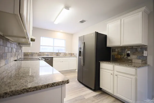 a kitchen with stainless steel appliances granite countertop a refrigerator a sink a stove and white cabinets with wooden floor