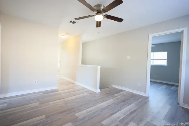 an empty room with wooden floor ceiling fan and windows