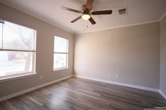 an empty room with wooden floor fan and windows