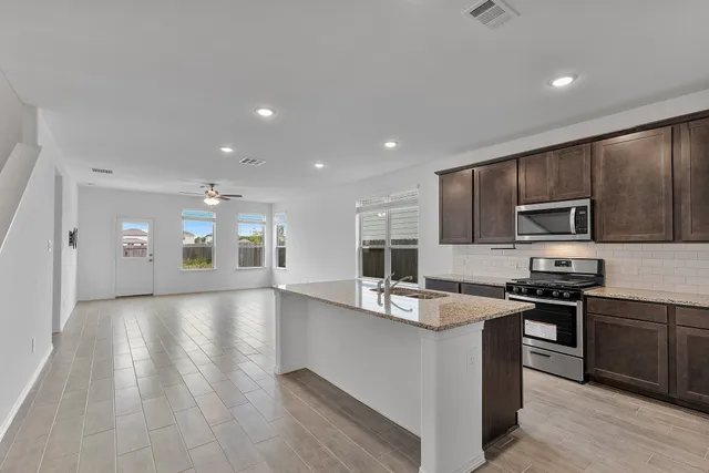 a kitchen with stainless steel appliances granite countertop a sink dishwasher a stove top oven a refrigerator with grey cabinets and wooden floor