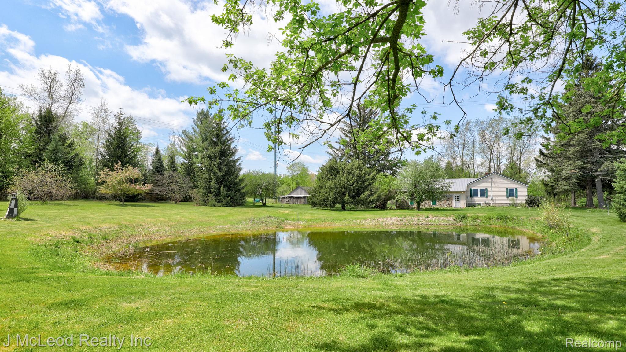 69 West Snover Road Mayville, MI 48744 - Photo 40 of 46 Expansive lawn with a central pond feature, surrounded by mature trees and lush greenery