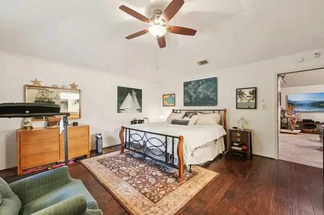 a spacious bedroom with a bed a dresser and wooden floor