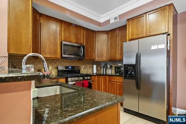 a kitchen with stainless steel appliances granite countertop a refrigerator a stove and a sink with wooden cabinets
