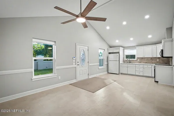 a view of an empty room with kitchen and window