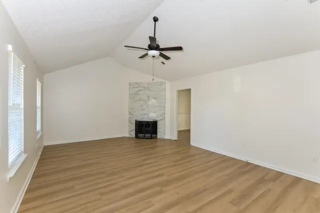 a view of an empty room with chandelier fan and wooden floor