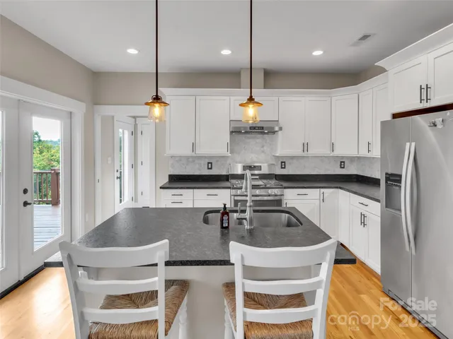 a kitchen with kitchen island stainless steel appliances a sink a stove a refrigerator cabinets and chairs