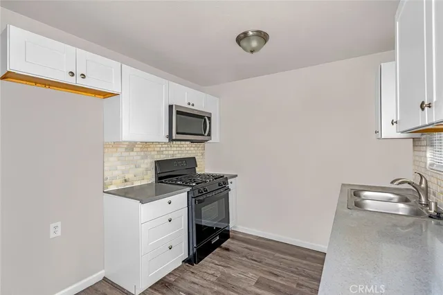 a kitchen with granite countertop a stove top oven a sink dishwasher and a microwave with wooden floor